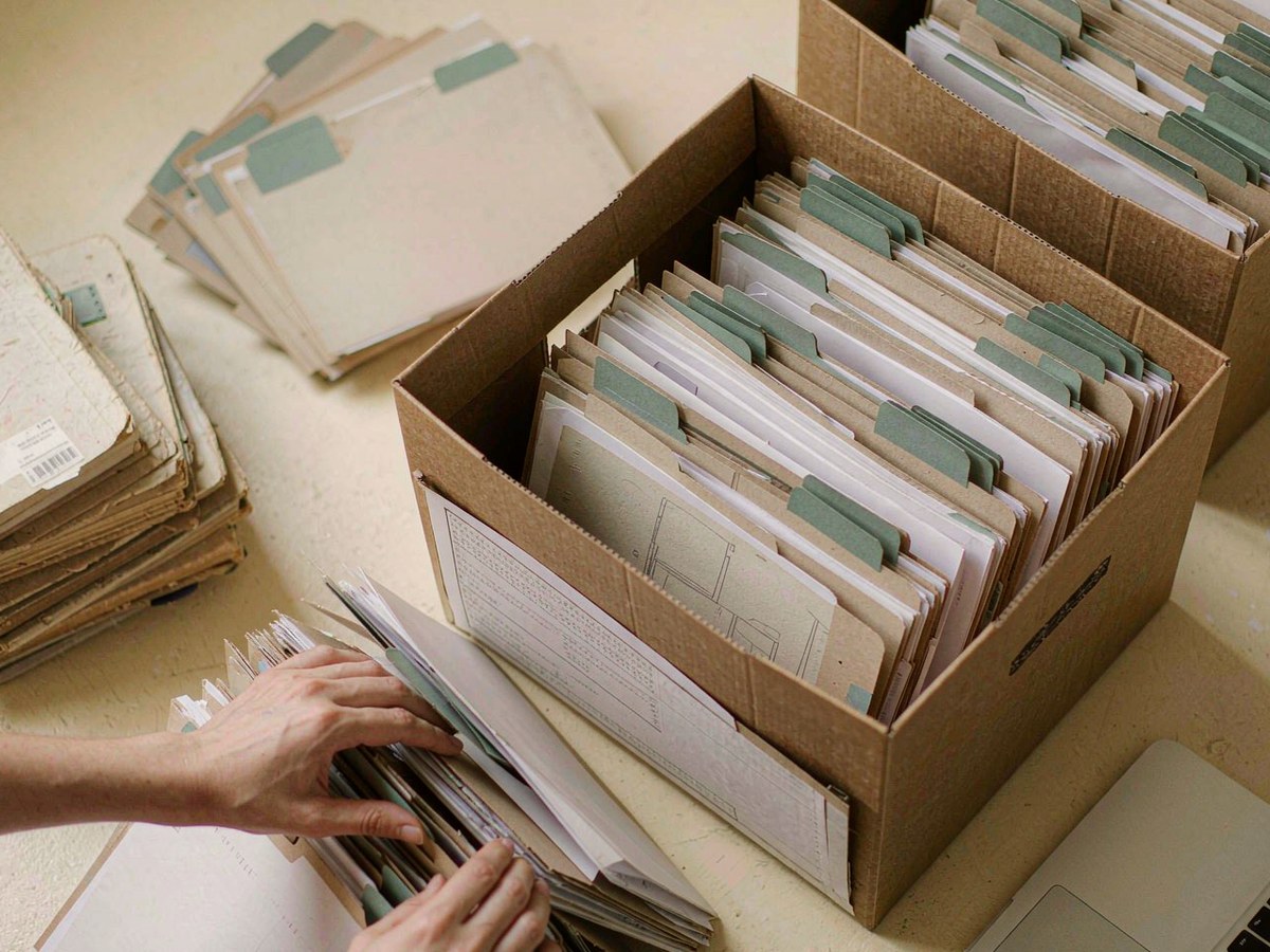 Archive boxes and folders being sorted, with a laptop at the edge of the desk